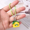 Dettaglio di un ciondolo a forma di casa gialla con tetto verde e cordino intrecciato - Verde