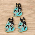 Dettaglio di tre ciondoli smaltati con gatto nero su foglie colorate su base in legno - Stile Gatto / Confezione da 10 / Blu