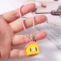 Dettaglio del ciondolo a forma di casa gialla con cinturino intrecciato per borsa - Rosa