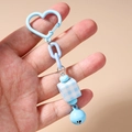 Détail du porte-clés bleu en forme de cœur avec un cube à carreaux et une petite cloche - Bleu