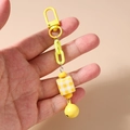 Détail du porte-clés à grosse chaîne jaune avec perle cubique à damier et petite clochette - Jaune