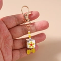 Détail d'un porte-clés artisanal en perles avec cube floral et ruban jaune vif - Nœud