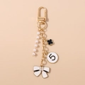 Dettaglio di un portachiavi dorato con perle bianche, quadrifoglio nero e fiocco elegante - Oro