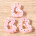 Macro detail of pink resin heart charms with colorful sequins on wood background - Letter B