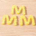 Close-up of three yellow resin letter M pendants with glitter on a wooden surface - 5 Pieces / M