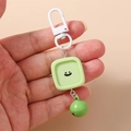 Détail d'un pendentif carré vert avec visage souriant, clochette et crochet blanc en plastique - Style Carré / Vert