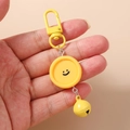 Detalle de llavero amarillo de carita sonriente con cierre de langosta y cascabel de metal - Forma Redonda / Amarillo