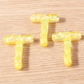 Detailed macro of three translucent resin T-letter pendants with yellow sequins for DIY - 5 Pieces / Letter T
