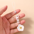 Detail of cartoon fried egg phone charm with yellow smiley face held in hand - Poached Egg Shape / White