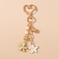 Dettaglio del portachiavi a cuore con perline e ciondoli dorati a forma di stella e fiori - Stella marina