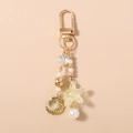 Detalle de un llavero dorado temático marino con perlas, caracola y estrella de mar - Estrella de mar blanca