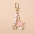 Detalle de un llavero dorado con estrella de mar de resina rosa y cuentas de perlas - Estrella de Mar Rosa
