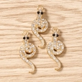Detalle de tres colgantes de serpiente dorados con diamantes de imitación sobre madera - Dorado