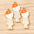 Vista de detalle de tres dijes de calavera blanca con sombreros naranjas sobre madera - Paquete de 10 / Dorado Blanco Naranja