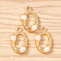 Dettaglio di tre ciondoli ovali dorati martellati con smalto rosa per gioielli fai-da-te - Oro Rosa