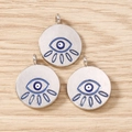 Detailed close-up of three silver evil eye charms with blue enamel on wood surface - 10 Pieces Pack / Silver Blue