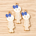 Three gold skull charms with blue bows and white enamel on a light wood surface - 10 Pieces Pack / Gold White Blue