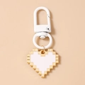 Close-up of pixel art heart keychain with gold metal frame and white enamel filling - White