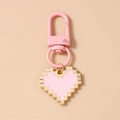 Macro detail of pixelated heart keychain with pink alloy drip oil and golden metallic trim - Pink