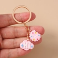 Close-up of pink cloud and biscuit charms on a gold keychain held by hand - Pink