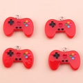Macro shot of four red resin gamepad pendants with silver metal rings on a pink background - Red