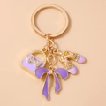 Dettaglio di ciondoli a borsa e scarpette viola con strass su portachiavi dorato - Viola