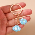 Close-up of light blue cloud and biscuit pendants on a gold-tone keyring charm - Sky Blue