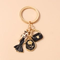 Detalle de llavero dorado con figura de mujer, bolso negro y disco grabado con una rosa - Dama Bolso Negro