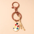 Detailed view of paintbrush and colorful artist palette charms on a gold keychain - Dark Coffee