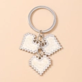 Macro shot of mosaic pixel heart keychain with three charms on a polished silver ring - White