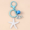 Detalle de colgante de ballena azul con estrella de mar y cascabel en llavero de metal - Estrella de Mar Azul