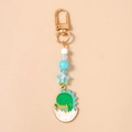 Close-up of cute green dinosaur enamel keychain with star beads and golden lobster clasp - Green Dinosaur