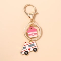 Detail eines goldenen Schlüsselanhängers mit rosa Arztkoffer und Krankenwagen-Anhängern - Rosa medizinische Box Krankenwagen