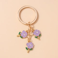 Macro view of gold metal keychain featuring purple enamel roses and crystal accents - Purple