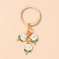 Close-up of golden rose keychain featuring white enamel flowers and crystal accents - White