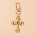 Close-up of golden gothic cross keychain with hollow patterns and green gemstone - Gold Cross