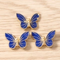 Detailed close-up of blue enamel butterfly pendants with gold beaded edges for DIY jewelry - Blue