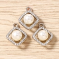 Macro view of three square rhinestone geometric pendants with white pearls on wood surface - Silver