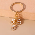 Detalle de llavero de metal dorado con dijes de esmalte blanco con diseño de número 5 - Blanco