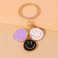 Detail of colorful enamel smiley face charms on a golden keychain keyring - Black White Purple