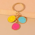 Detail of colorful smiley face pendants on a polished gold keyring with three enamel charms - Yellow/Blue/Pink