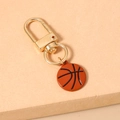 Detail of a basketball keychain with golden lobster clasp on a textured display stand - Calico