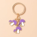 Detalle de llaveros de setas púrpuras con anillos dorados y lunares blancos en fondo rosa - Morado