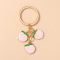 Detail eines goldenen Schlüsselanhängers mit drei pfirsichfarbenen Emaille-Anhängern - Rosa