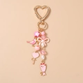 Nahaufnahme der rosa Vogel-, Herz-Lollipop- und Blumen-Emaille-Anhänger am goldenen Schlüsselbund - Herz Schleife Blumenstrauß