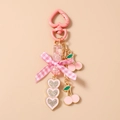Detail of pink bow keychain with cherry pendant and rhinestone hearts on cream background - Pink