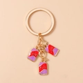 Detail eines goldenen Schlüsselanhängers mit rot-violetten Emaille-Coladosen-Anhängern - Lila