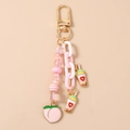 Detalle de dijes de té con leche rosa y colgantes de corazón en un llavero dorado - Bebida de Durazno Rosa