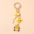 Detailed close-up of a golden keychain with yellow bear charm and pearl beads accessory - Orange