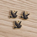 Three gold-plated swallow charms with black enamel finish on a light wood surface - Black